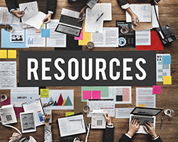image looking down at people seated around a desk working on computers with paperwork scattered around with the word Resources over it